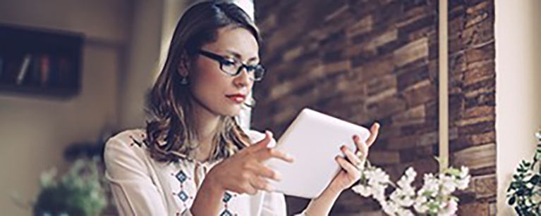 A woman in glasses reading on her tablet.