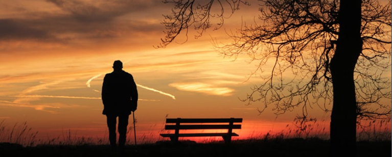 An elderly man in a park watching the sunset.