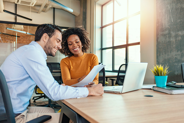A man and women laughing while looking at a document together in an office