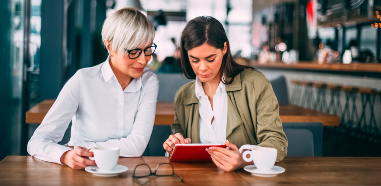 Two women sitting side by side looking at a tablet. 