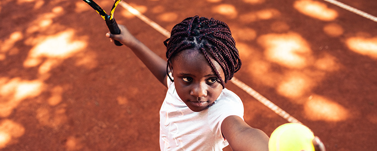 A girl serving a tennis ball with a racket on a clay tennis court Link to title: News and Articles page