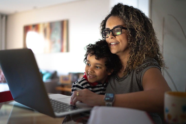 A mum hugging her son whilst they look at a laptop.