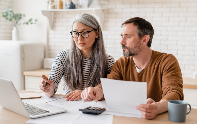 A woman and man looking at documents and a laptop at a desk together.