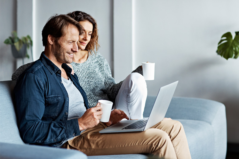 Couple drinking coffee and sitting on a couch while looking at a laptop