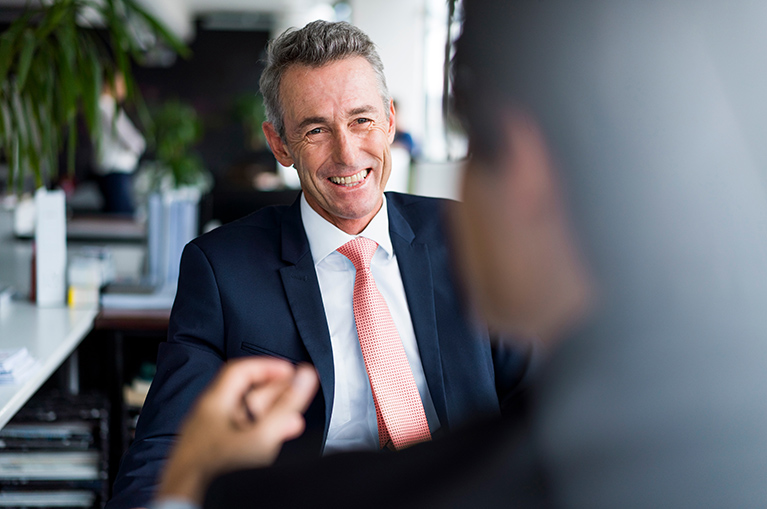 A man smiles at someone sitting across from him during a business meeting. 