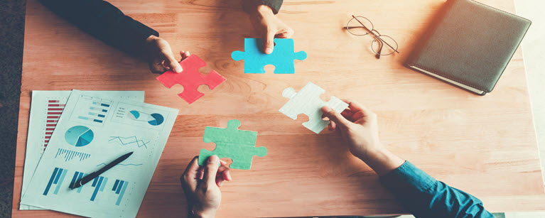 Hands holding puzzle pieces over financial charts, symbolizing strategic planning and collaboration toward financial goals.