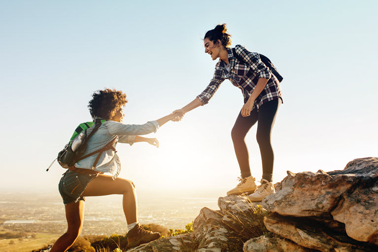 A woman helping another woman climb the mountain.