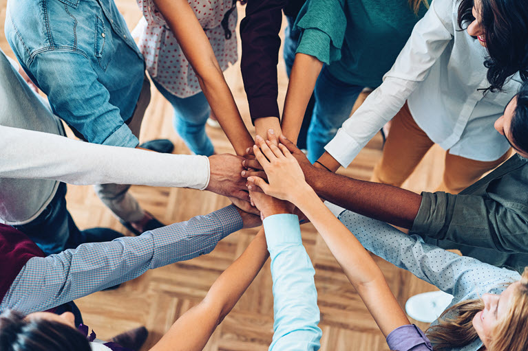 Several colleagues joining hands in a circle symbolizing teamwork.