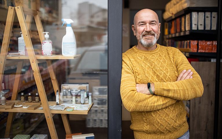 Photo of a business owner in the door frame of his store. The window also shows a few products for sale.