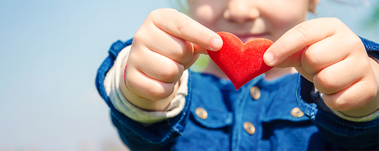  A child holding a red heart, representing the Chartier Grandmaison Leclerc Team’s dedication to community engagement and social causes.