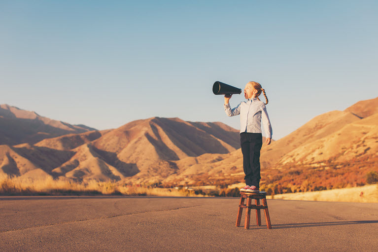 A girl standing on a stool shouting into a megaphone in the desert.