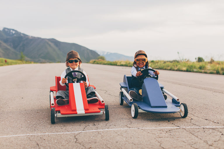Two children in blue and red go-karts in the countryside.