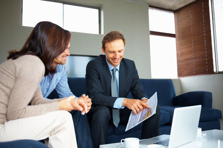 A man showing a man and woman a document. They are sitting on sofas.