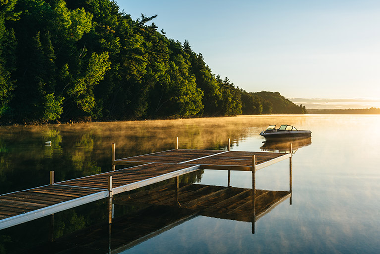 A boat and a dock on a lake with a sunrise