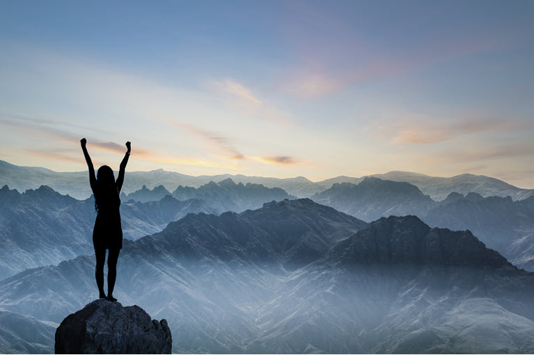 A confident woman standing on top of a mountain at dawn.