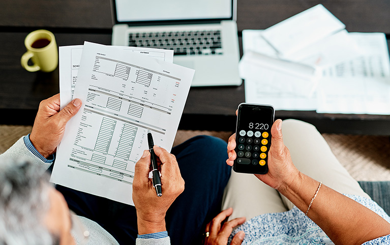 A person holding a pen and sheets of paper and another person holding a calculator.