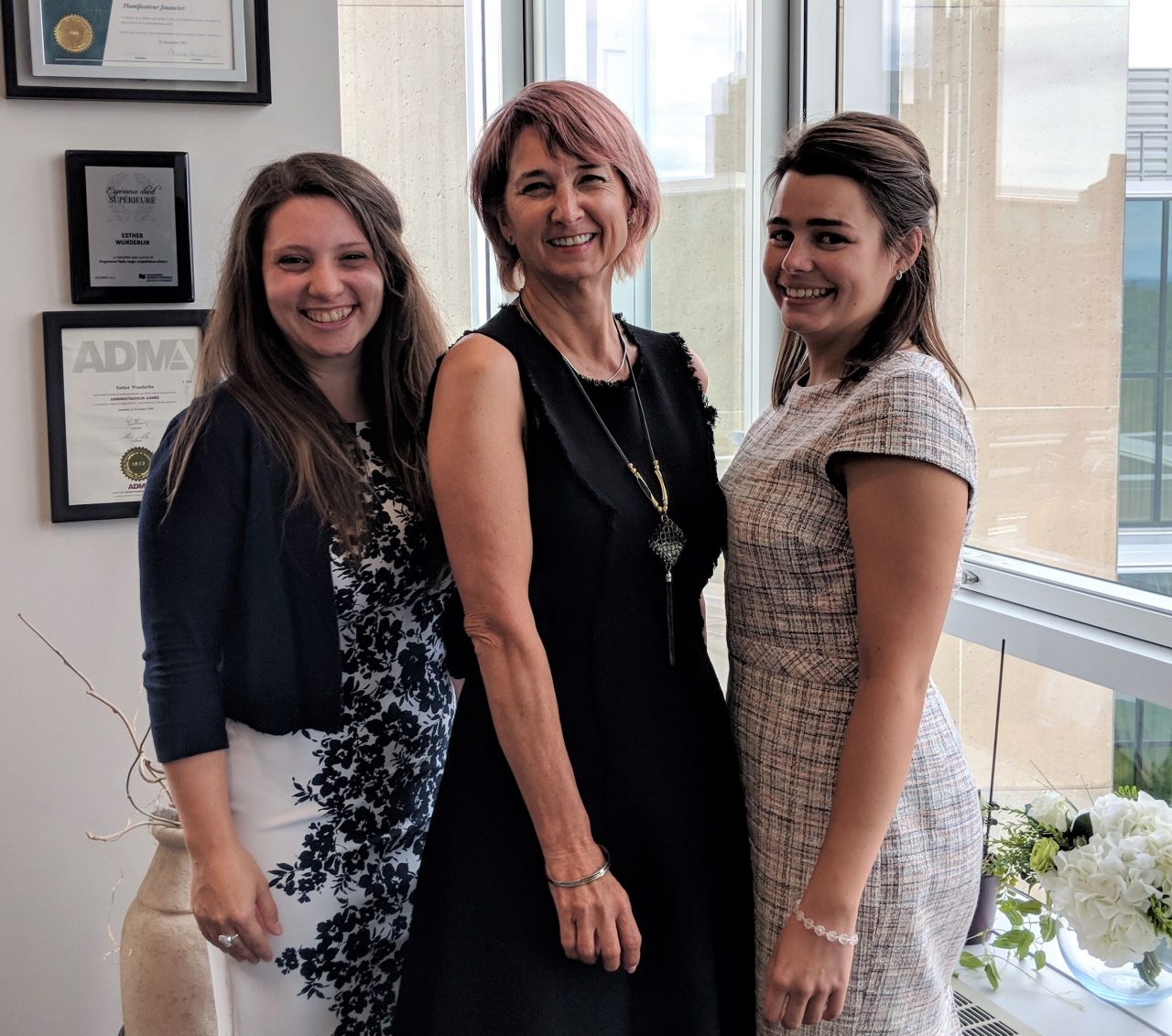 Three woman standing next to a window and smiling.