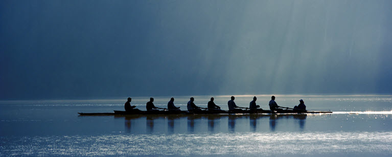 Eight rowers in a boat on calm water with a serene blue background and rays of light shining through.