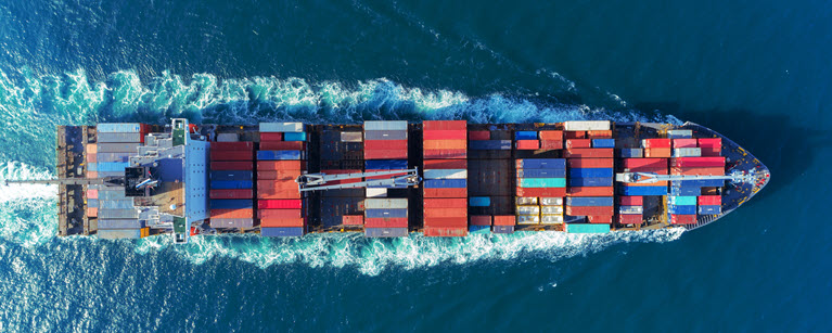 Aerial view of a cargo ship with colorful containers sailing through deep blue ocean waters. 
