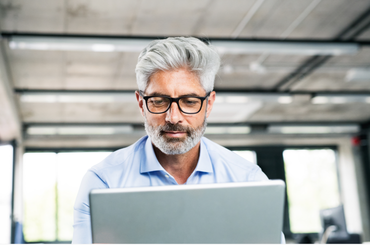 Man with grey hair and glasses using a laptop
