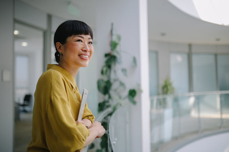 A woman with a tablet in a modern office with plants and glass walls.