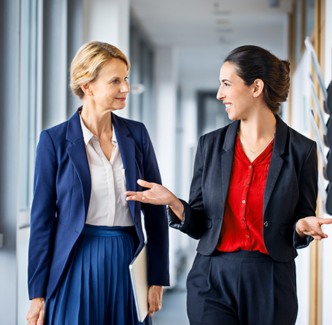 Two women are talking as they walk down a corridor in an office.